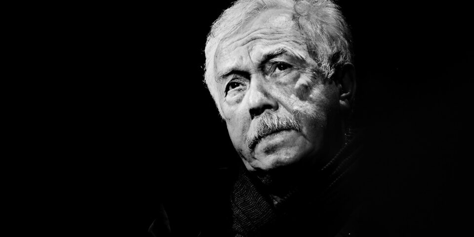 Slajd: Czarno-białe zdjęcie starszego mężczyzny z jasnymi włosami i wąsami. Oświetlona jest tylko twarz. Tło czarne.