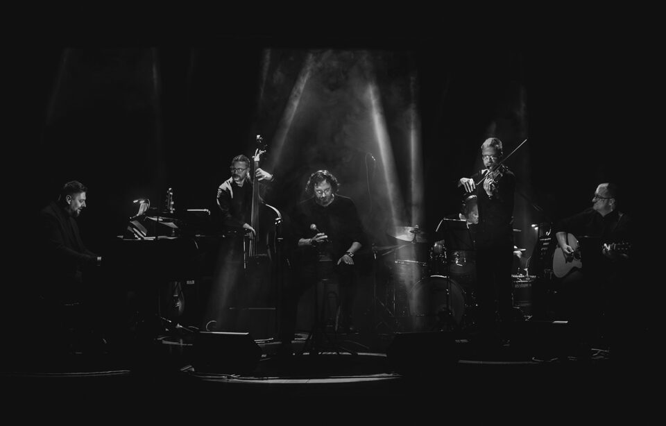 Zdjęcie sześcioosobowego zespołu muzycznego na scenie.