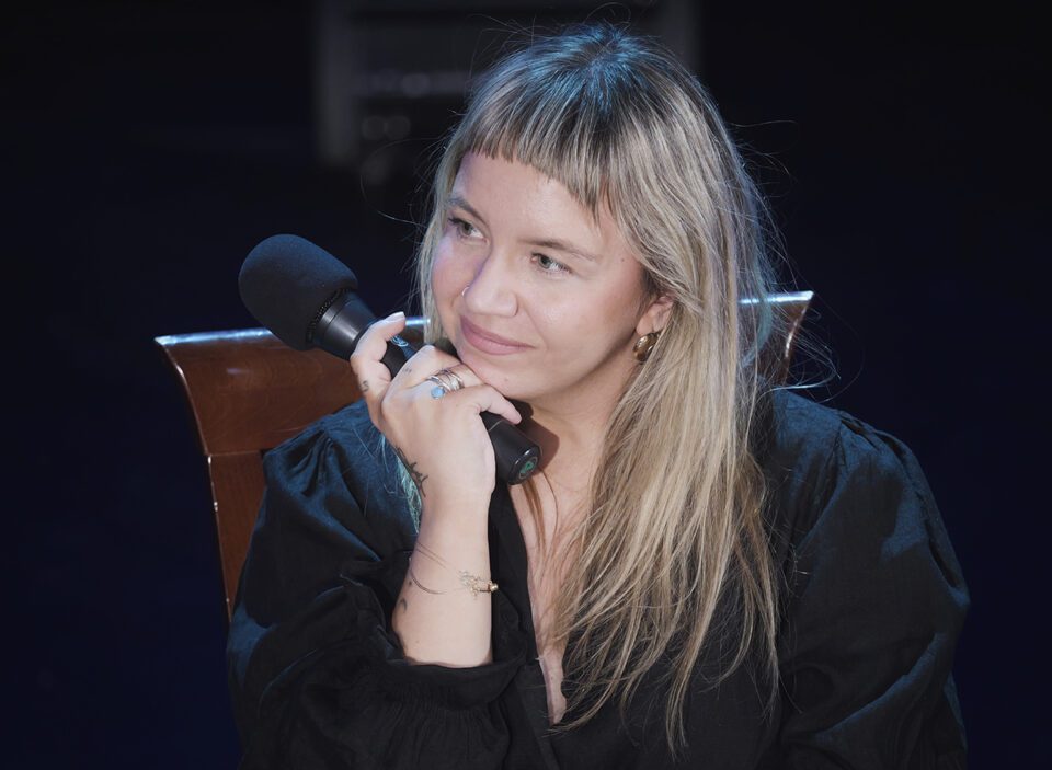 Portret Mai Chitro; kobieta jest zasłuchana, zerka na jednego z rozmówców, który jest poza kadrem.