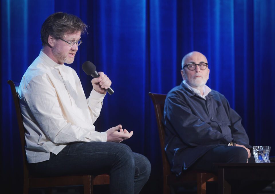 Aleksander Laskowski i Michał Kwieciński podczas rozmowy, Laskowski trzyma mikrofon przy twarzy, Kwieciński zerka na rozmówcę.