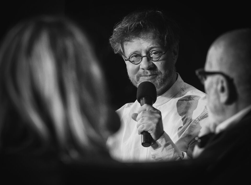 Zbliżenie na Laskowskiego podczas rozmowy; mężczyzna ma mikrofon w dłoni; na twarzy maluje mu się pogodny uśmiech.