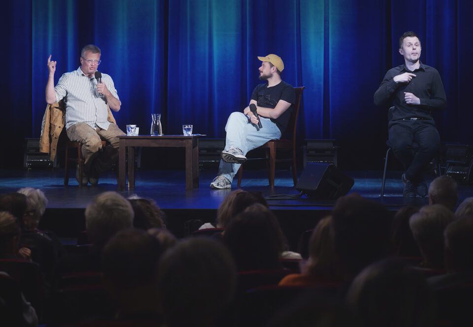 Zdjęcie zrobione z perspektywy widowni; na pierwszym planie rzędy z publicznością; nie ma wolnych miejsc; Meller i Szot rozmawiają, obok nich tłumacz PJM.