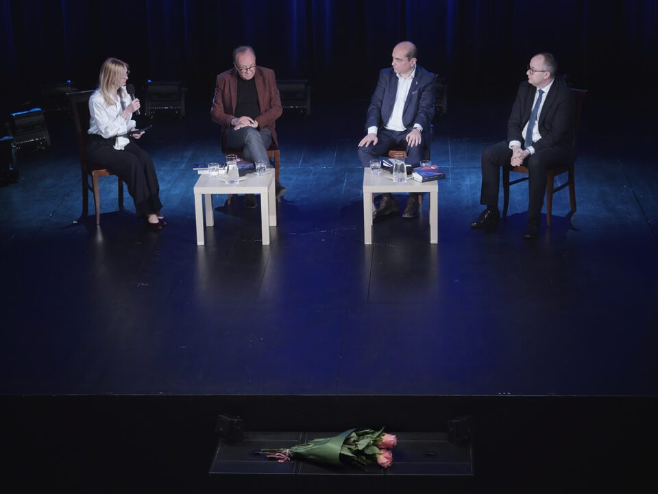 Zdjęcie wykonane podczas rozmowy o książce Kerskiego, na scenie od lewej: prowadząca spotkanie - prof. Iwona Hofman, prof. Traba, Kerski i Minister Bodnar. Wszyscy siedzą na krzesłach na środku sceny; przed nimi, na skraju sceny bukiet różowych róż.