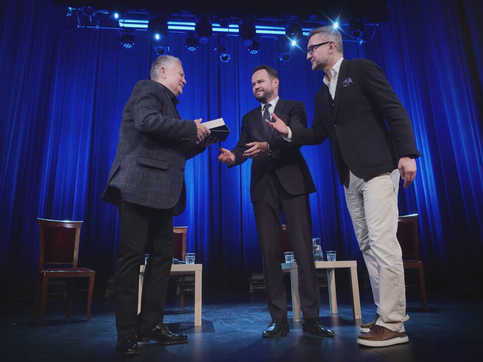 Andrzej Peciak podczas przyjmowania medalu z rąk Wojewody Lubelskiego, Krzysztofa Komorskiego, wręczenie ma miejsce na scenie teatru; asystuje przy tym Dyrektor Teatru, Michał Karapuda.