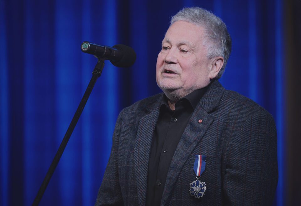 Andrzej Peciak z przypiętym medalem "Zasłużony Kulturze Gloria Artis" podczas przemowy na scenie teatralnej.