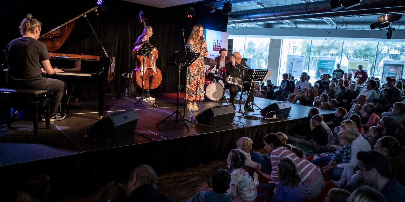 Slajd: Zespół muzyczny na scenie. Pianista, saksofonista, wokalistka, kontrabasista i perkusista. Przed sceną publiczność, w tym dużo dzieci.